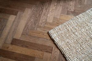 An upclose picture of wood flooring in a chevron pattern with a rug on it
