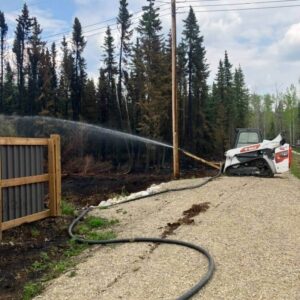 A Bobcat skid steer holding a fire hose during Peace Region wildfire season