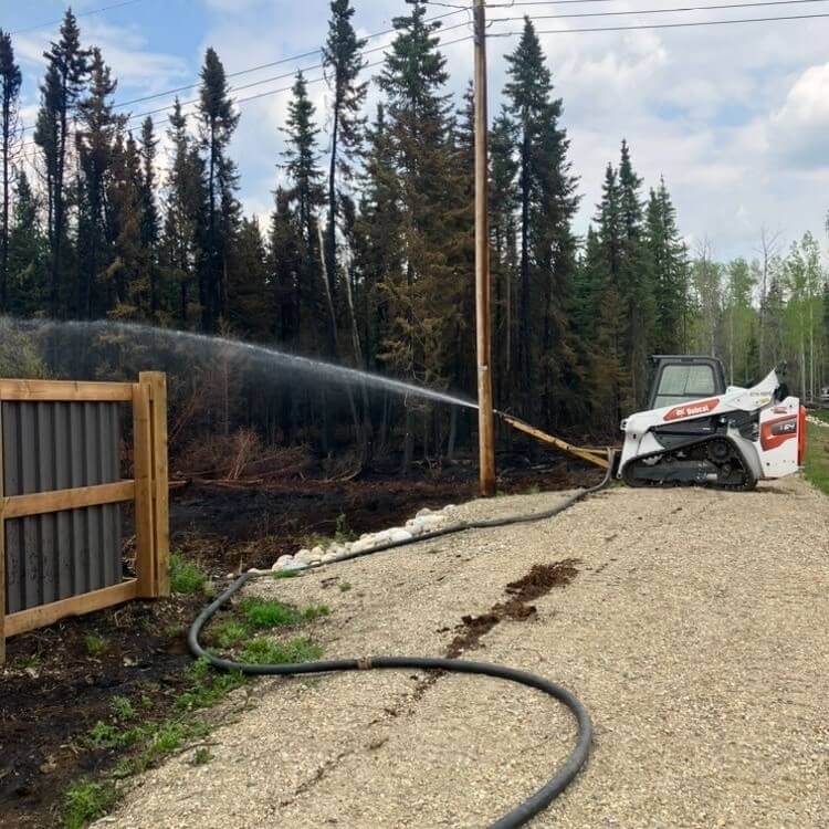 A Bobcat skid steer holding a fire hose during Peace Region wildfire season